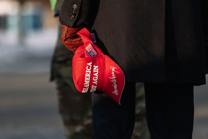 Person holding a red Make America Great Again hat, representing an ex-Trump fan facing ICE detention issues.