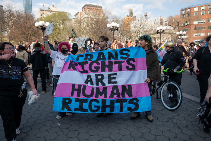 Protesters holding a trans rights banner amidst a crowd, highlighting clashes with MAGA ideologies on dates.