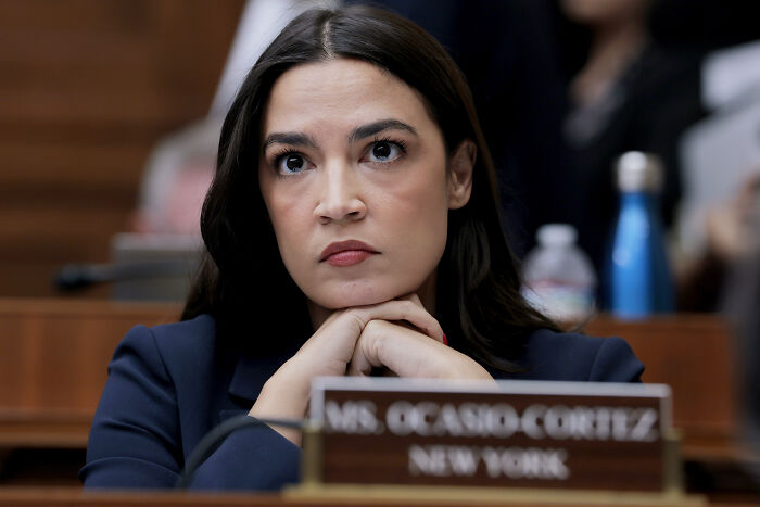 Alexandria Ocasio-Cortez in a navy blazer, focused and thoughtful, signaling potential 2028 White House run.