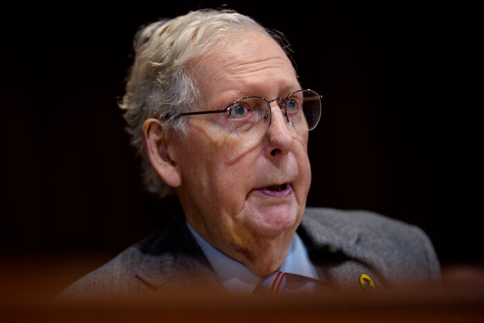 Senator Mitch McConnell speaking at an event, wearing glasses and a suit, sparking term limit debate discussion.