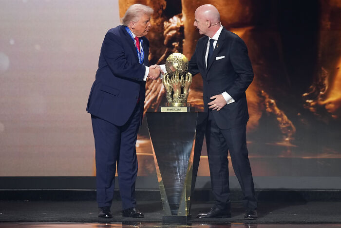 Donald Trump receiving champion of beautiful clean coal trophy on stage, shaking hands with man in black suit.