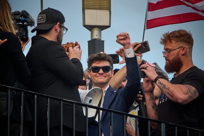 JD Vance raising fist at event, surrounded by supporters and media capturing moment with phones.