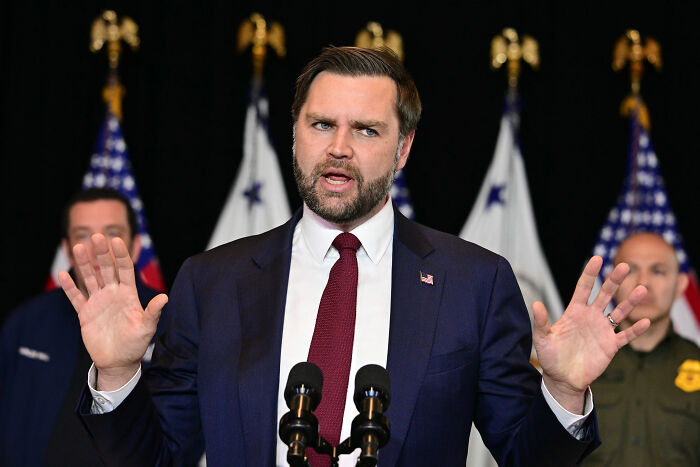 JD Vance speaking at a podium with American flags behind him, making a statement about Trump shooter Thomas Crooks.