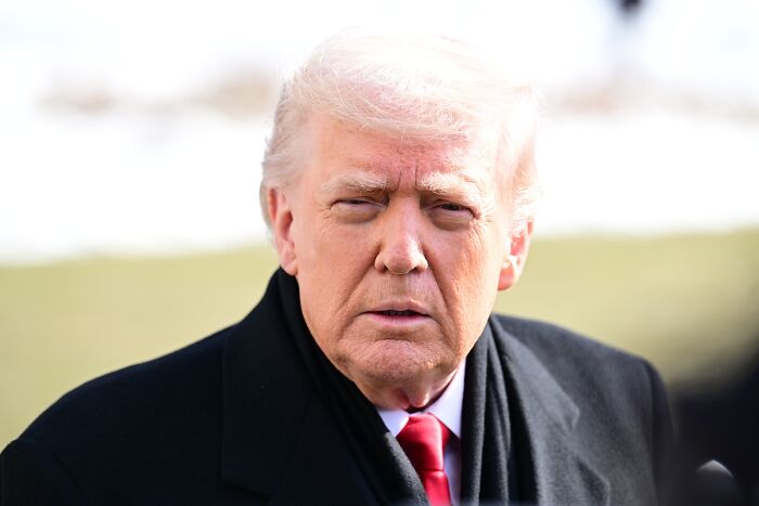 Donald Trump outdoors wearing a black coat and red tie with Epstein emails revealing concerns about dementia after 2017 dinner.