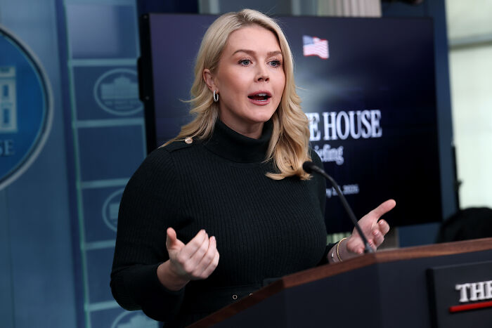 Karoline Leavitt speaking at a podium in the White House briefing room, addressing a press conference.