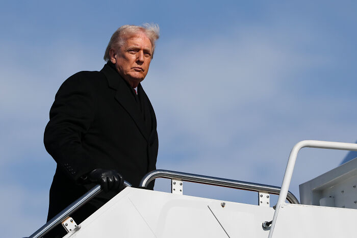 Donald Trump wearing black coat and gloves, boarding plane with Kennedy Center closure and repairs context.