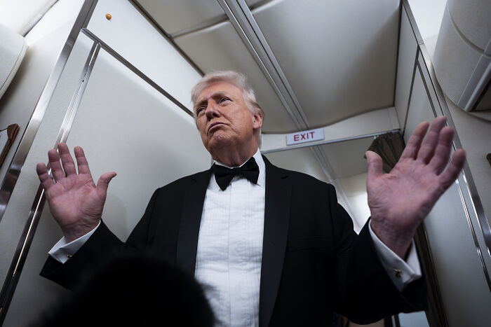 Former President Donald Trump in a black tuxedo raising hands inside an airplane, related to women revealing MAGA ideologies on dates.