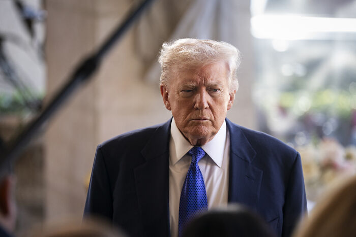 Former president Donald Trump in a suit with a blue tie, appearing serious amid discussions involving Republicans and political tensions.