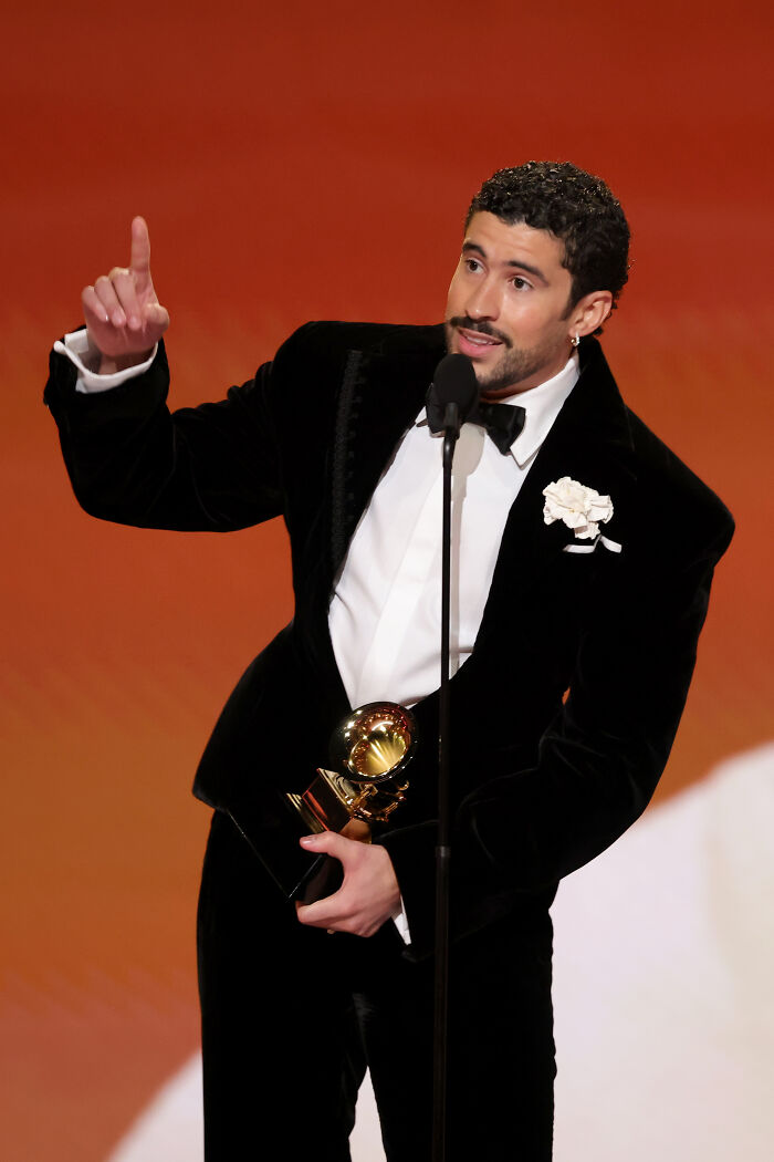Male star at the Grammys holding an award and speaking out against ICE during acceptance speech on stage.