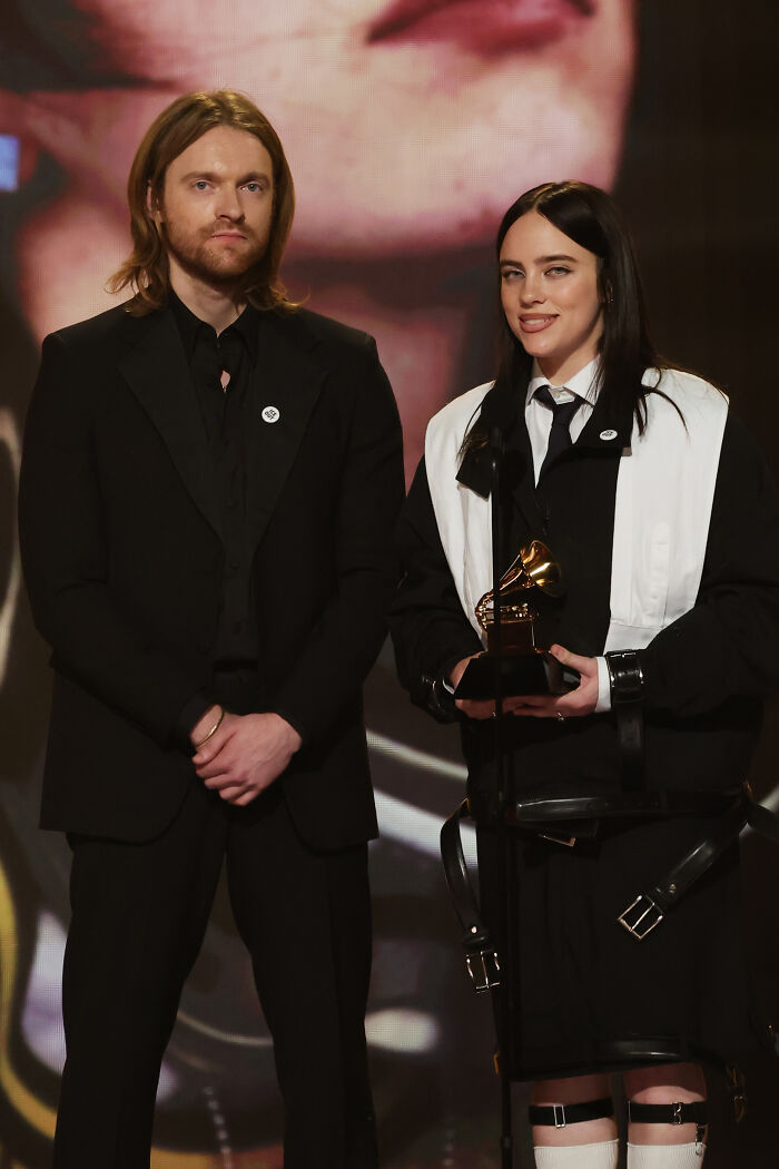 Two stars on stage holding a Grammy, speaking out against ICE during the Grammys event.