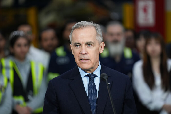 Canadian Prime Minister speaking at podium, reacting to B.C. school attack that claimed nine lives, with blurred audience behind.