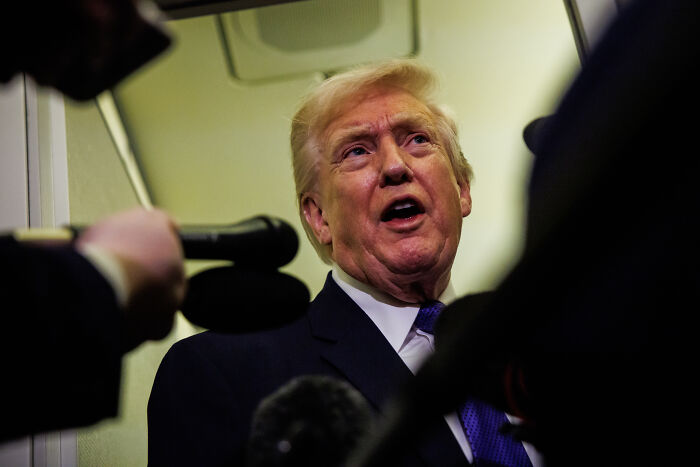 Donald Trump speaking to reporters at an event, showing signs he skipped makeup, resulting in an odd appearance.