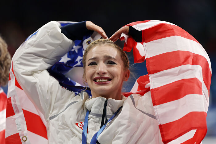 U.S. Olympic athlete showing mixed emotions wrapped in American flag after winning a medal at the games.