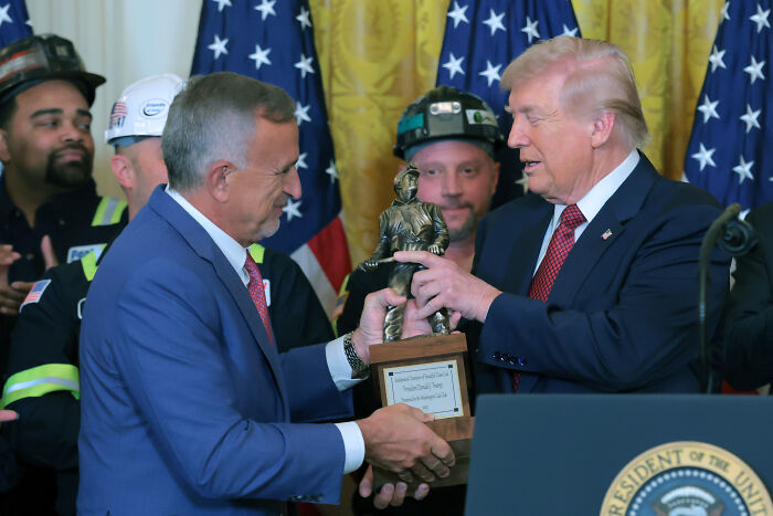 Donald Trump receiving the Champion of Beautiful Clean Coal trophy during a ceremony with coal industry workers present.