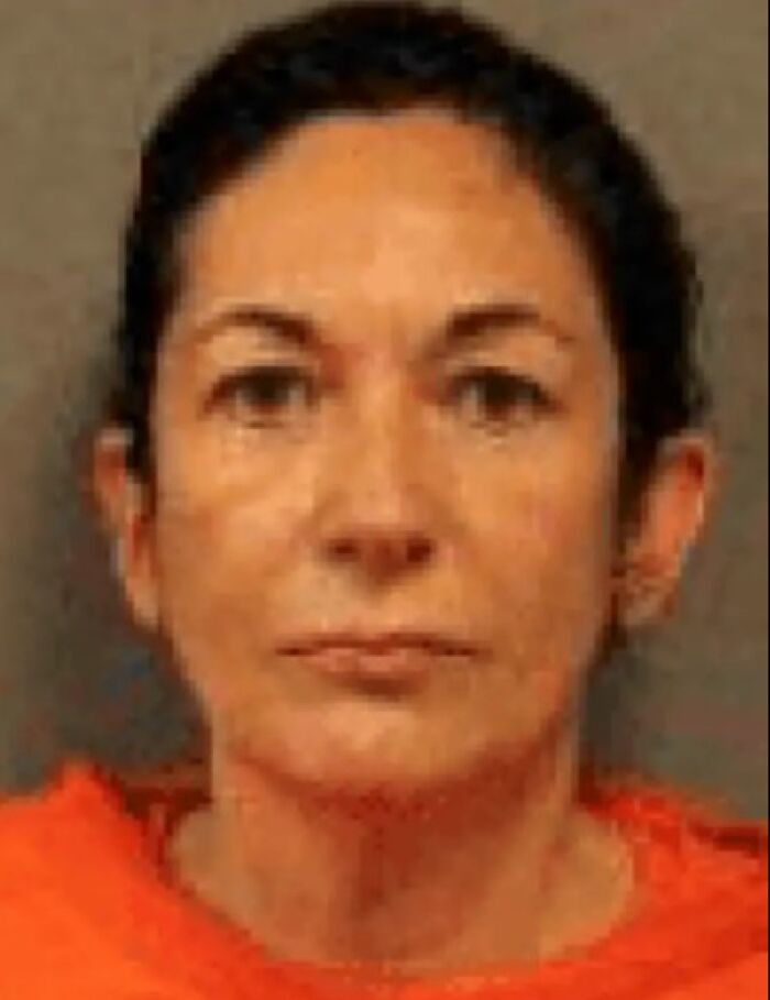 Mugshot of Ghislaine Maxwell wearing an orange prison uniform with a neutral expression inside a detention cell.