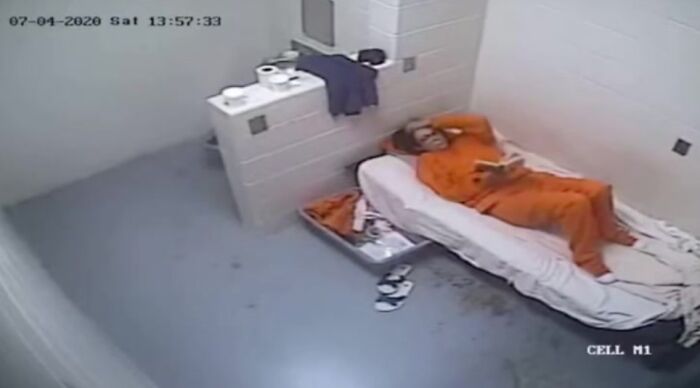 Surveillance image of Ghislaine Maxwell in her prison cell wearing orange jumpsuit with items scattered around the bed.