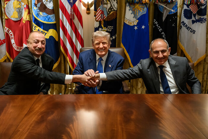Three men shaking hands in front of American flags, related to JD Vance&rsquo;s Armenia post deletion issue.