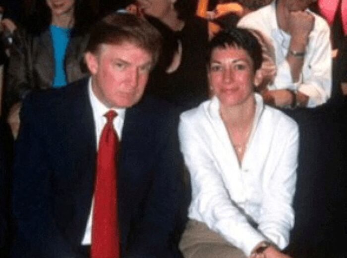 Blurry image of two people sitting closely, with one wearing a dark suit and red tie, the other in a white shirt.