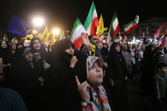 Crowd waving Iranian flags at nighttime rally during Iran conflict