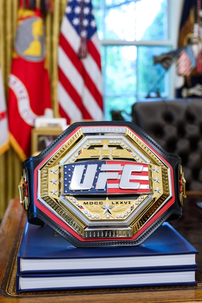 Close up of UFC championship belt in Oval Office with flags in background