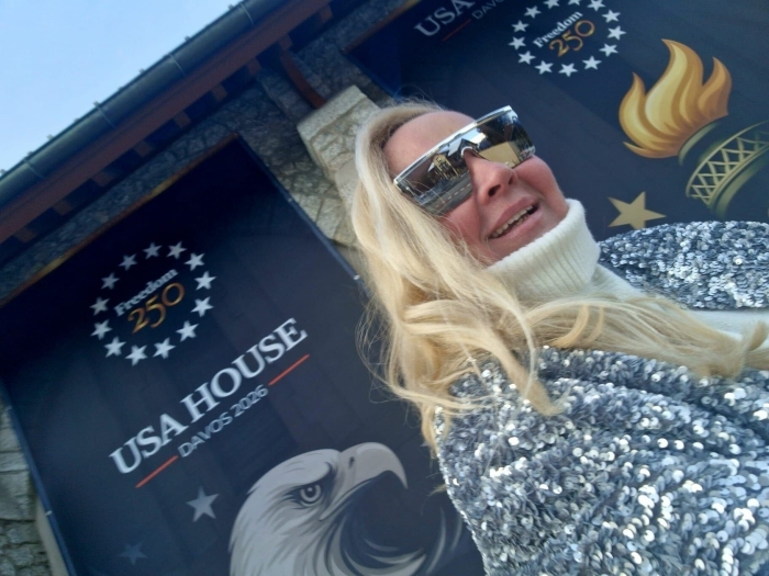 A blonde woman in sunglasses smiles, with a USA House Davos 2026 banner in the background.
