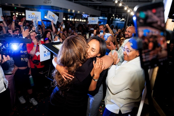 A democratic socialist candidate embraces a woman amidst a cheering crowd, celebrating unseating a Denver Democrat.