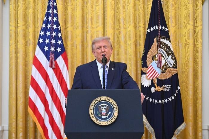 Trump election bombshell: Donald Trump at a podium in front of American and presidential flags, addressing the crowd.